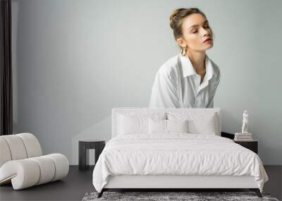 young sensual woman with closed eyes wearing white shirt and black latex pants and sitting on cube isolated on grey. Wall mural