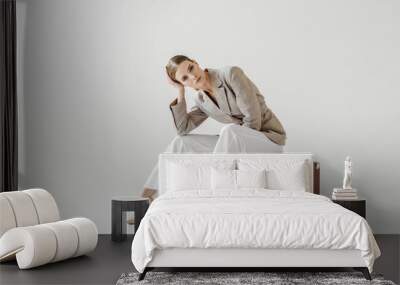 young stylish female model in linen jacket sitting on vintage suitcase and looking at camera isolate Wall mural