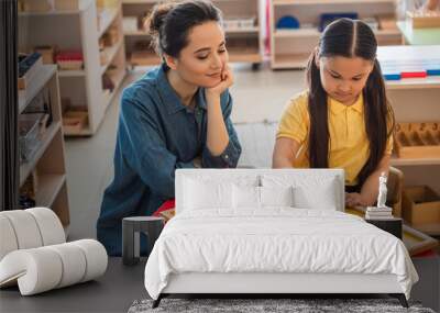 young teacher looking at asian child combining earth map puzzle in montessori school Wall mural