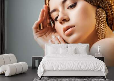 young tender naked woman with shiny makeup, golden rings and earrings in turban isolated on grey Wall mural