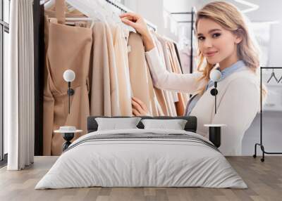 Young woman holding hanger with clothes in showroom Wall mural