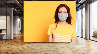 young woman in medical mask looking at camera on yellow Wall mural