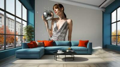 young woman in trendy top and leather pants holding chain with disco ball on grey. Wall mural