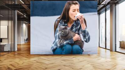 young woman with allergy holding facial tissue and british shorthair cat at home Wall mural