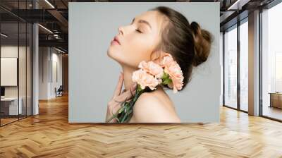 Young woman with carnations touching neck isolated on grey. Wall mural