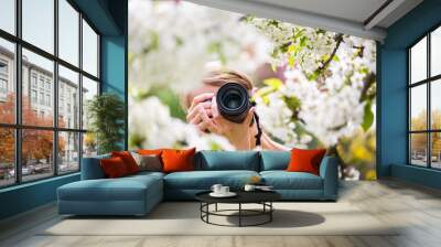 Pretty, female photographer outdoors on a lovely spring day, taking pictures of a blossoming tree Wall mural