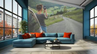 traveling in nature, woman photographing alpine landscape with her smartphone Wall mural