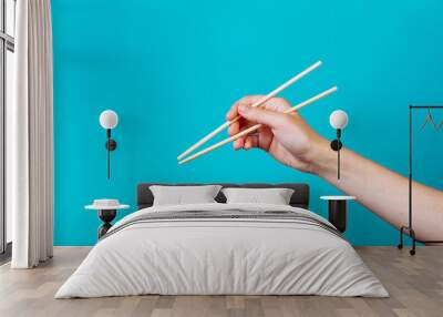 Hands holding chopsticks. Isolated on blue background, the place for caption and text Wall mural