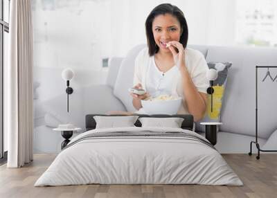 Cute young dark haired woman in white clothes eating popcorn whi Wall mural