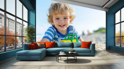 A cheerful young child with blonde curly hair plays with a colorful toy car on a sandy beach.  Wall mural