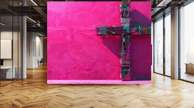 A contemporary art piece featuring a cross made from recycled materials, set against a vivid pink background. Wall mural