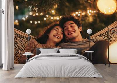 Joyous Asian couple lying in hammock, laughing together. Wall mural