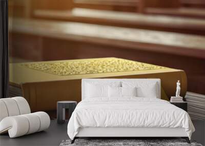 Prayerful Patterns: A simple Catholic prayer book rests on a wooden bench in an empty chapel, its gold-embossed cover catching the light. Wall mural