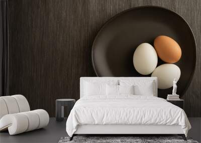 One brown and two white eggs are on black plate and gray tablecloth Wall mural