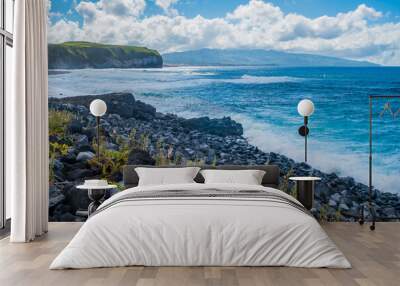 Plants on volcanic rocks with sea waves crashing with mountains on the horizon on Santa Bárbara beach, São Miguel - Azores PORTUGAL Wall mural