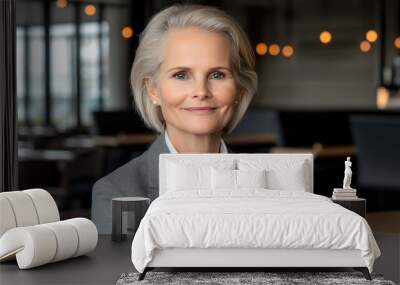 A businesswoman with blonde hair smiles gently, sitting at an outdoor table in a restaurant, wearing a light gray suit and exuding confidence and warmth Wall mural