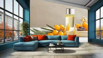 A glass bottle filled with sea buckthorn essential oil rests on a wooden board beside fresh yellow berries, all illuminated by soft natural light Wall mural