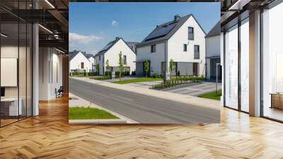 A row of modern, white houses with solar panels on their roofs are situated on a quiet residential street. The houses are surrounded by green lawns and landscaping Wall mural