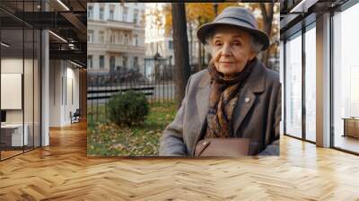 An elderly woman with a scarf smiles at the camera while sitting on a bench, bathed in warm golden hour light amid vibrant autumn colors Wall mural