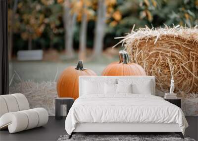 Colorful pumpkins of various sizes rest on stacks of hay bales, showcasing fall harvest beauty in a serene farm setting surrounded by greenery Wall mural