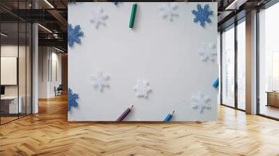 This flat lay features colored snowflakes surrounded by colored pencils on a white background, inviting children to engage in creative winter coloring activities Wall mural