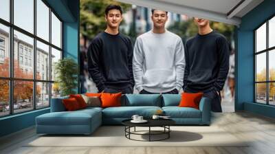 Three male models in black sweatshirts and slacks pose confidently in an urban location, highlighting their stylish look against a softly blurred city background Wall mural