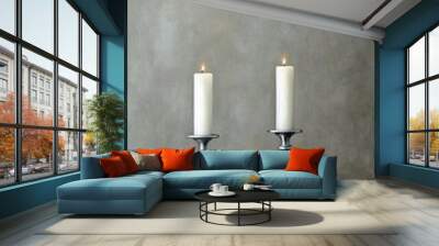 Two silver candlesticks with lit white candles sit on a table against a gray background, reflecting a minimalist aesthetic and adding tranquility to the space Wall mural