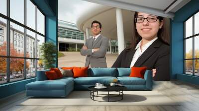 Two young professionals stand together in a contemporary office space, arms crossed, exuding confidence and focus under natural daylight Wall mural