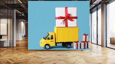 Yellow truck delivery gift box on blue background. Cargo transportation, delivery service. Transport company. Infrastructure and logistics. Unloading cardboard box. Copy space Wall mural