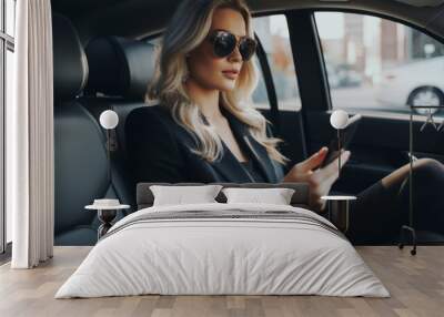 A beautiful young successful businesswoman uses a smartphone in the car during a trip, communicates with business partners, and types a message to friends and family. Wall mural