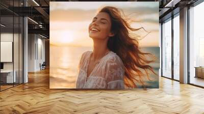 A happy beautiful young smiling woman with hair flying in the wind, having fun on the beach with her eyes closed at sunset. Golden Hour, Pleasure, Joy, Travel, Summer, Vacation concepts. Wall mural