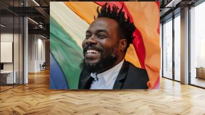 A man with a beard and a smile is standing under a rainbow flag Wall mural