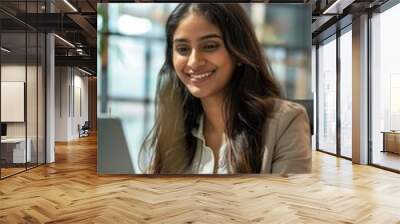 A woman is sitting at a desk and smiling while using a laptop Wall mural