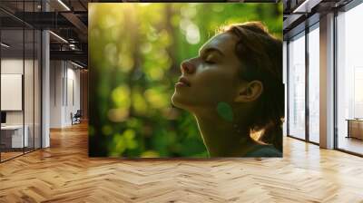 A woman is sitting in a forest, looking up at the sky Wall mural