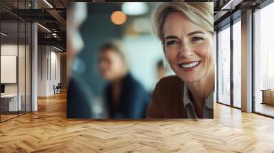 A woman with a smile on her face is sitting at a table with other people Wall mural