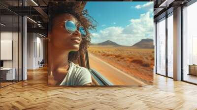 A woman with curly hair is driving down a road with mountains in the background Wall mural