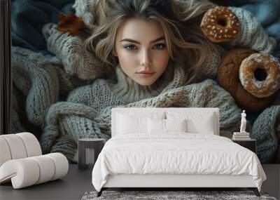 A young woman relaxes on a pile of cozy blankets, indulging in a book while enjoying donuts and the comforts of autumn Wall mural