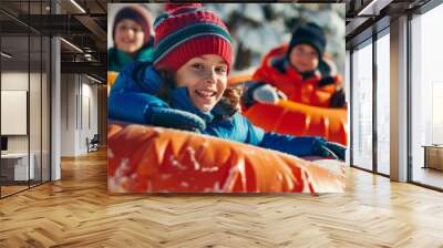 Children are laughing and smiling while tubing down a snowy hill, surrounded by tall trees and a bright winter sky Wall mural