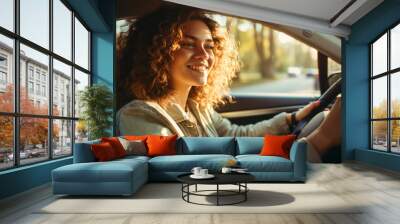 Close-up of a beautiful happy young curly-haired woman driving a car on a sunny day. Car purchase and rental, travel and vacation concepts. Wall mural