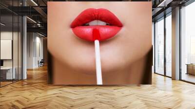 Close up portrait of attractive girl rouging her lips. She is holding red lipstick. Her mouth is gently open. Bright red lip gloss. Close-up, well-groomed, clean skin Wall mural