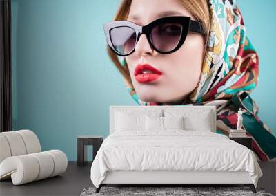 Fashionable portrait of a stylish young woman in sunglasses, isolated on blue background Wall mural