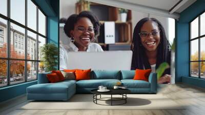 The two women share laughter and excitement as they engage with content on a laptop, surrounded by a vibrant and inviting workspace filled with plants Wall mural