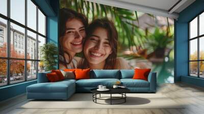 Two joyful women share a warm embrace surrounded by vibrant tropical foliage, radiating friendship and happiness in a sunny environment Wall mural