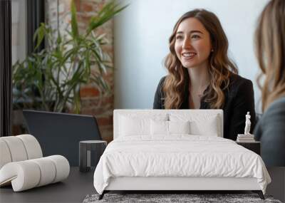 Two women are sitting at a table, one of them is typing on a laptop Wall mural