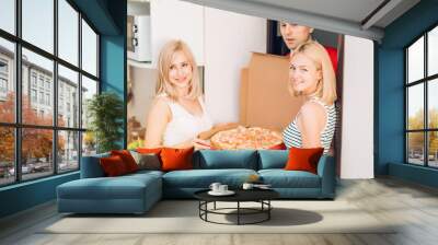 Two young caucasian woman receiving pizza from delivery man at home Wall mural