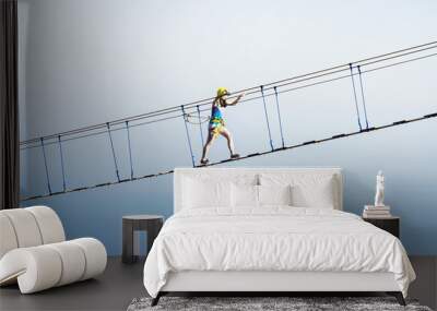 Young woman rising on hanging rope bridge at sea and sky background. Leisure extreme activity at summer day Wall mural