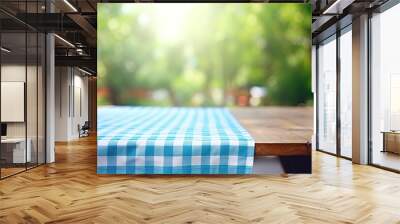 Wooden table with blue checked tablecloth and blurry green bokeh from kitchen window background. Perfect for summer and picnic-themed designs, especially for promoting food and drink products. Wall mural