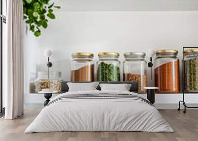 organized glass jars filled with spices herbs sit on white kitchen shelves Wall mural