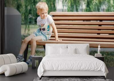 Small child plays in park. Kid is sitting on a park bench. Wall mural