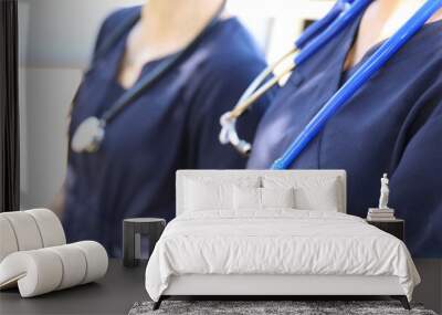 Two female medical practicioners in blue uniform with stethoscopes around their necks. Nursing or doctors in hospital gowns or clothes. Health, hospitals and medical themed image. Wall mural